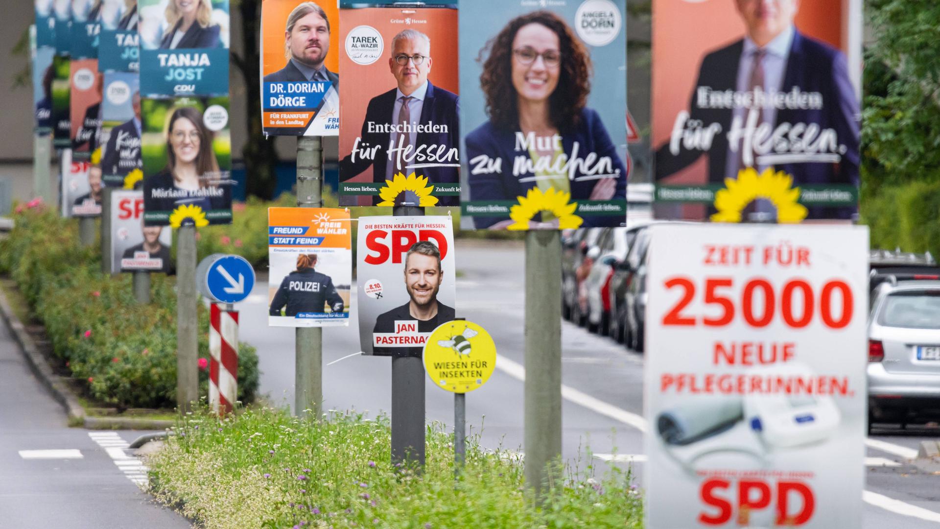 Wahlplakate aller Parteien hängen entlang einer vielbefahrenen Straße an Laternenpfählen.
