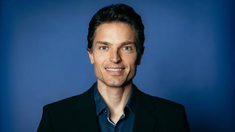 Enzo Weber posiert vor einem blauen Hintergrund für ein Pressefoto.