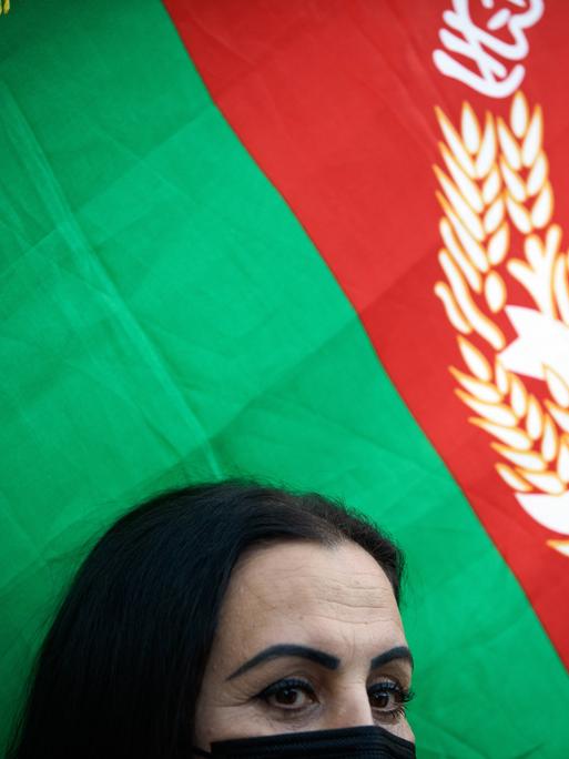 Eine Frau mit halbverschleiertem Gesicht, hinter ihr ist die afghanische Flagge zu sehen. 