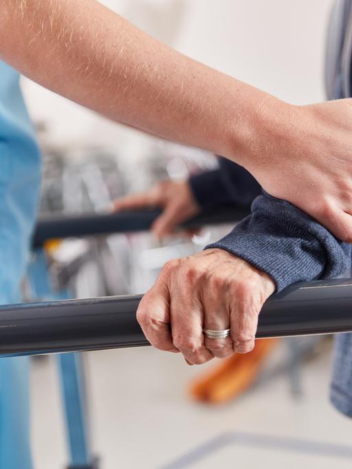 Hände einer Therapeutin stützen Patienten beim Lauftraining in der Physiotherapie 