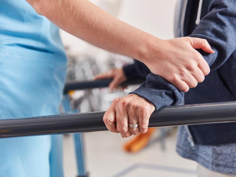 Hände einer Therapeutin stützen Patienten beim Lauftraining in der Physiotherapie 