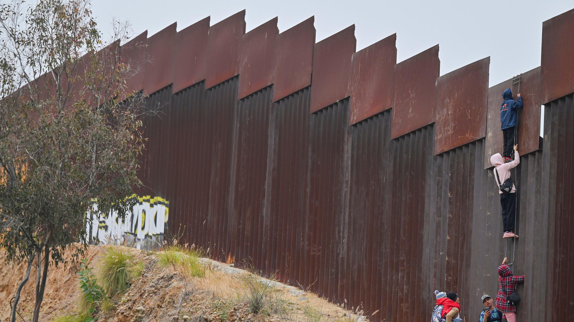 Eine kleine Gruppe von Migranten, darunter mindestens ein Kind, versuchen, mit einer Leiter über die Grenzmauer in die USA zu gelangen.