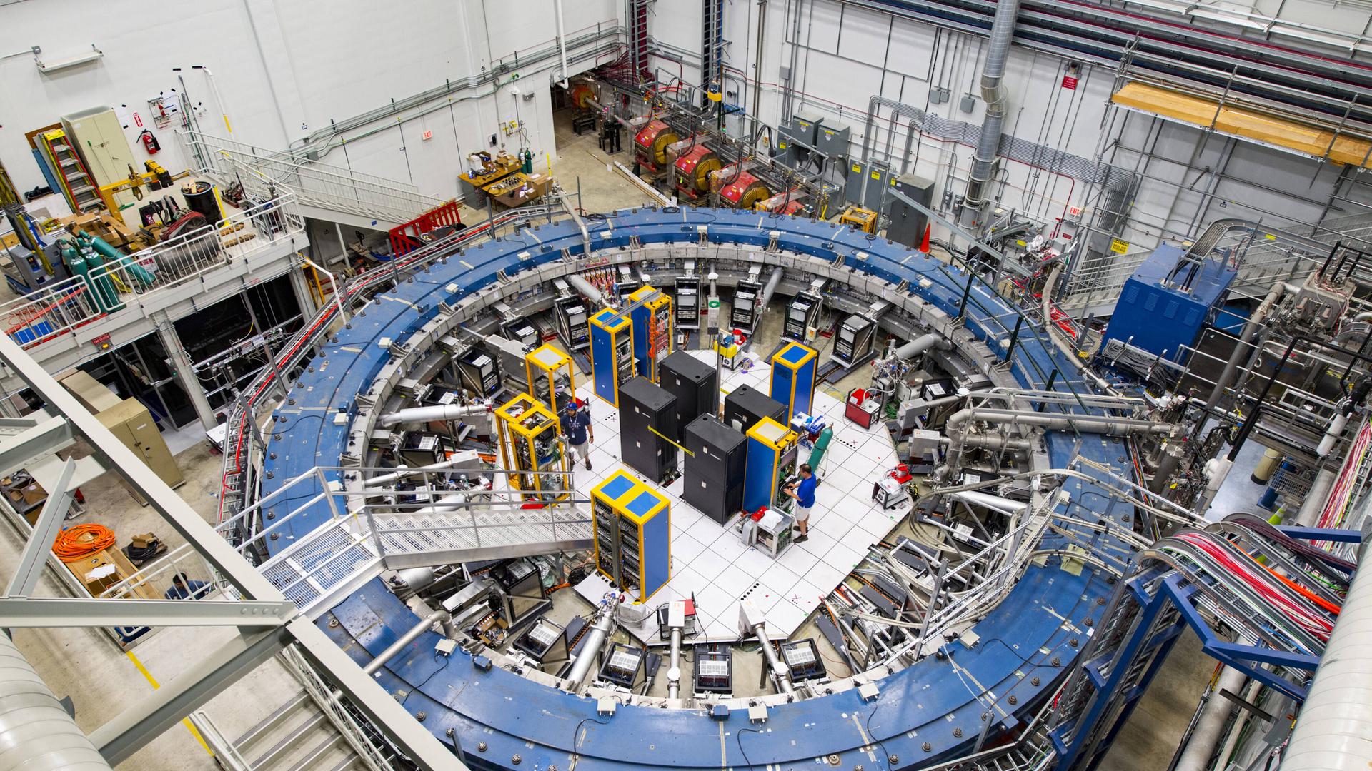 Der Teilchenbeschleuniger Myon-g-2-Ring inmitten anderer technischer Geräte in einer Halle.
