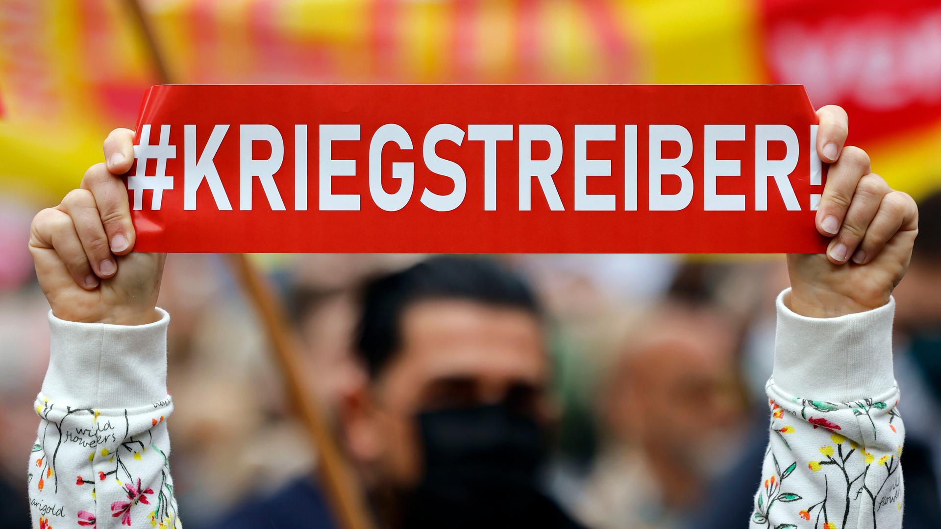 Ein Demonstrant gegen Kanzler Olaf Scholz hält ein Plakat mit dem Wort "Kriegstreiber!" in die Höhe auf der DGB-Veranstaltung am Tag der Arbeit auf dem Johannes Rau Platz. Düsseldorf, 01.05.2022 Ein Demonstrant gegen Kanzler Olaf Scholz hält ein Plakat mit dem Wort "Kriegstreiber!" in die Höhe auf der DGB-Veranstaltung am Tag der Arbeit auf dem Johannes Rau Platz. Düsseldorf, 01.05.2022