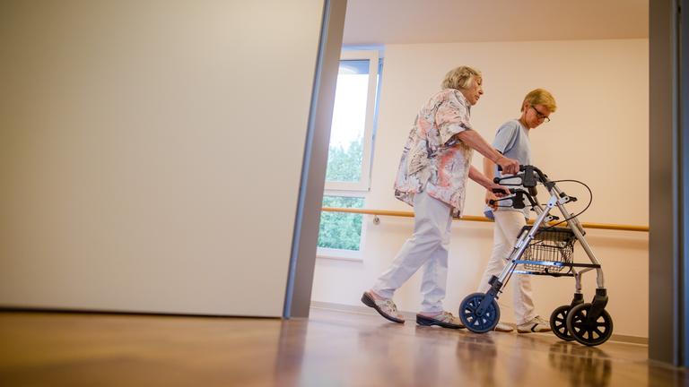 Debatte über Fachkräftemangel in der Pflege: Eine Pflegekraft geht in einem Pflegeheim mit einer älteren Dame über einen Korridor