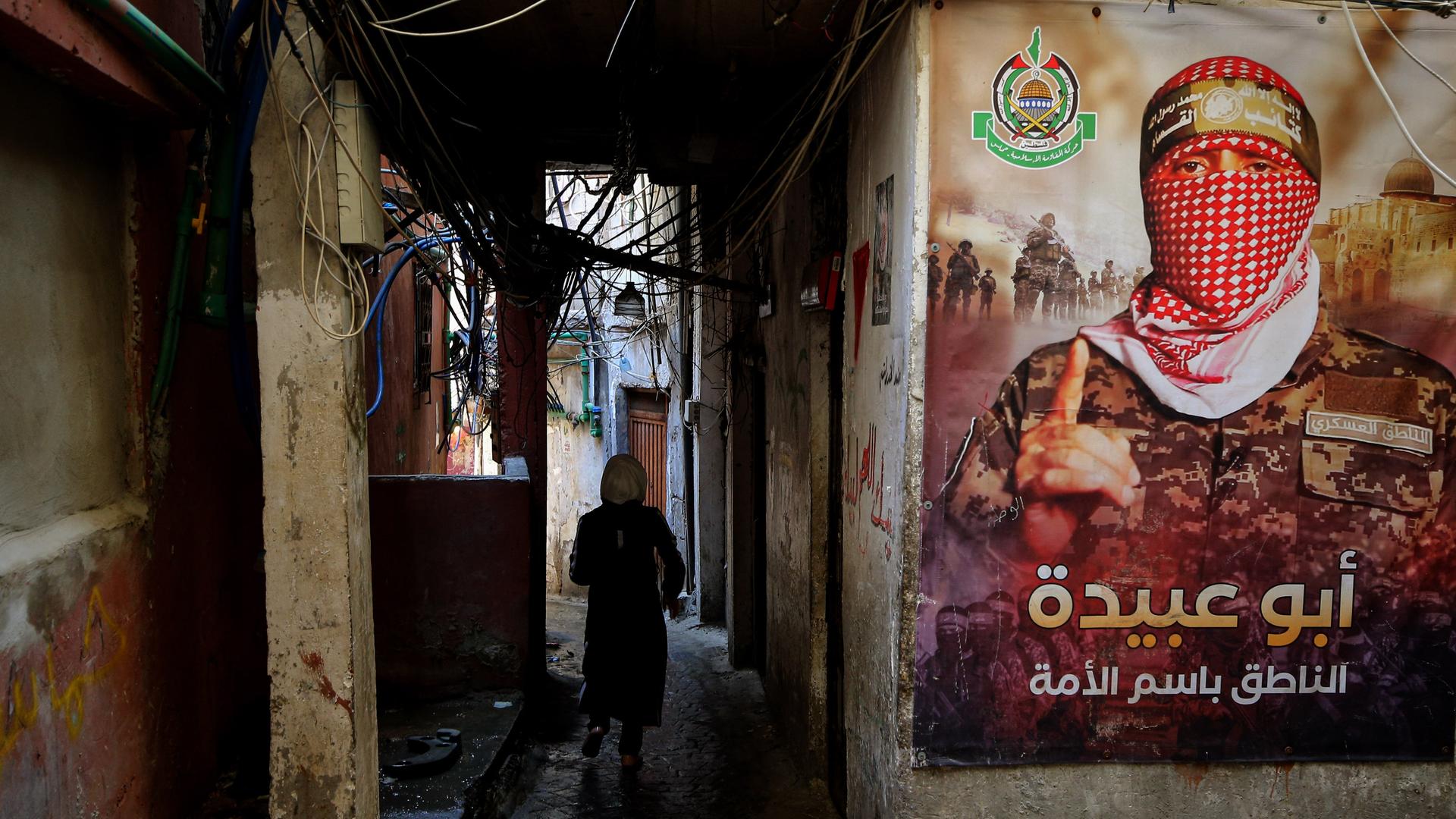 Ein palästinensischer Flüchtling geht durch eine enge Gasse im Beiruter Lager Burj al-Barjneh. An der Wand hängt ein Plakat mit dem Bild von Abu Obeida, dem Sprecher der Ezzedeen Al-Qassam-Brigaden der Hamas in Gaza.