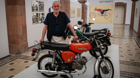 Der Gestalter Karl Clauss Dietel (1934-2022) steht in einer Ausstellung hinter einem Motorrad. 
