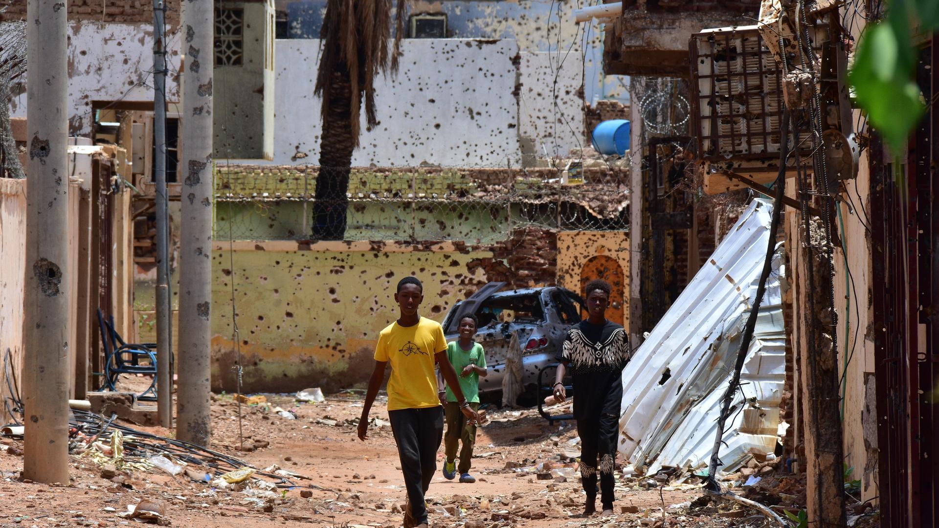 Jugendliche gehen im Sudan auf einer von Zerstörungen gezeichneten Straße entlang. 