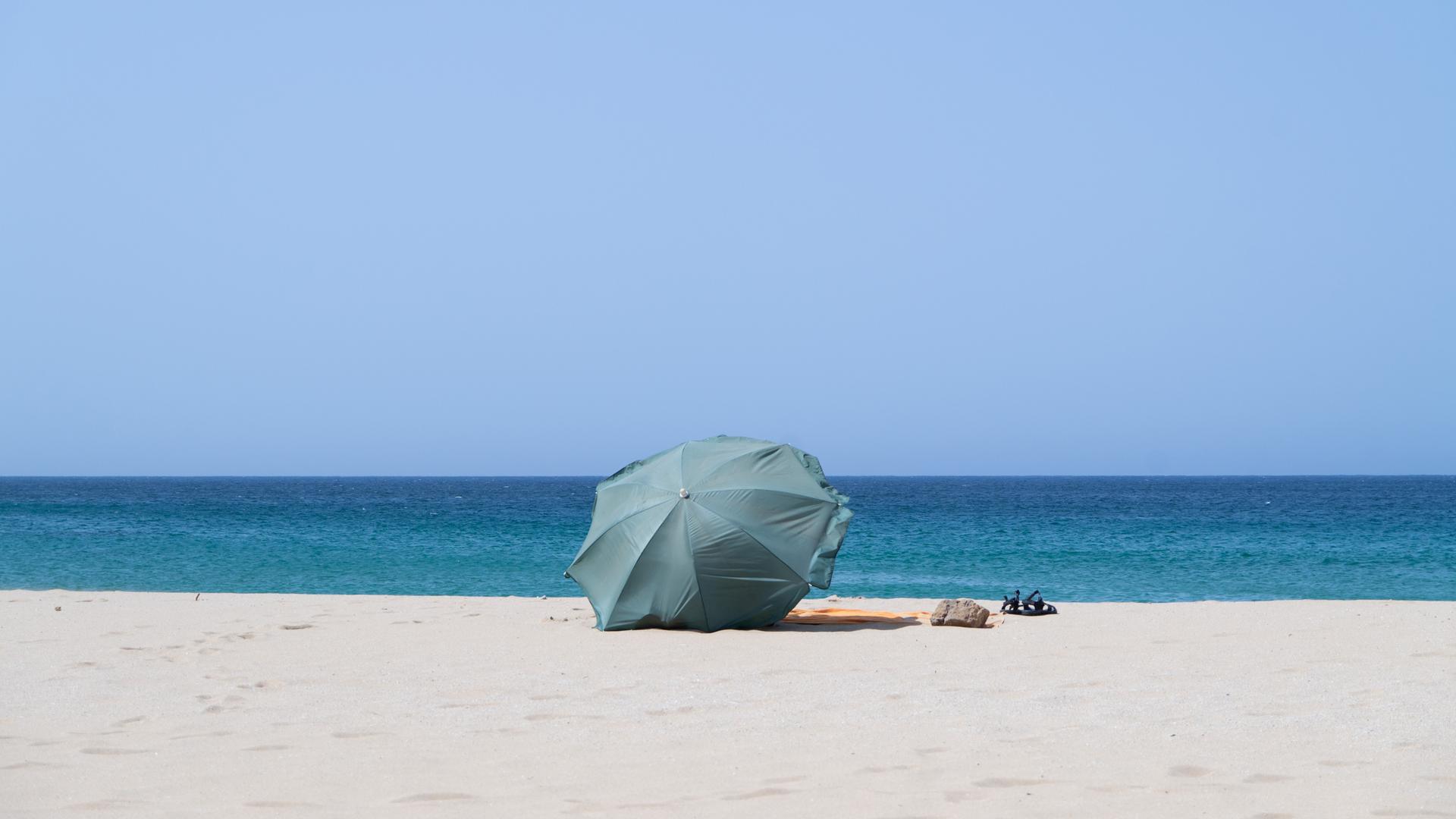 Ein grüner Sonnenschirm steckt im Sand an einem Strand..