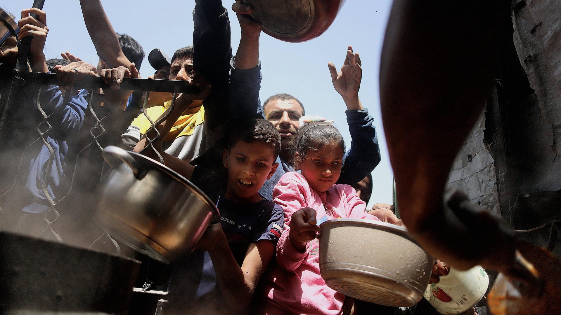 Menschen, Erwachsene und Kinder mit Schüsseln warten darauf, Hilfsgüter im Gazastreifen entgegenzunehmen. Menschen, Erwachsene und Kinder mit Schüsseln warten darauf, Hilfsgüter im Gazastreifen entgegenzunehmen.