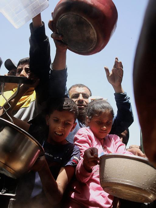 Menschen, Erwachsene und Kinder mit Schüsseln warten darauf, Hilfsgüter im Gazastreifen entgegenzunehmen.