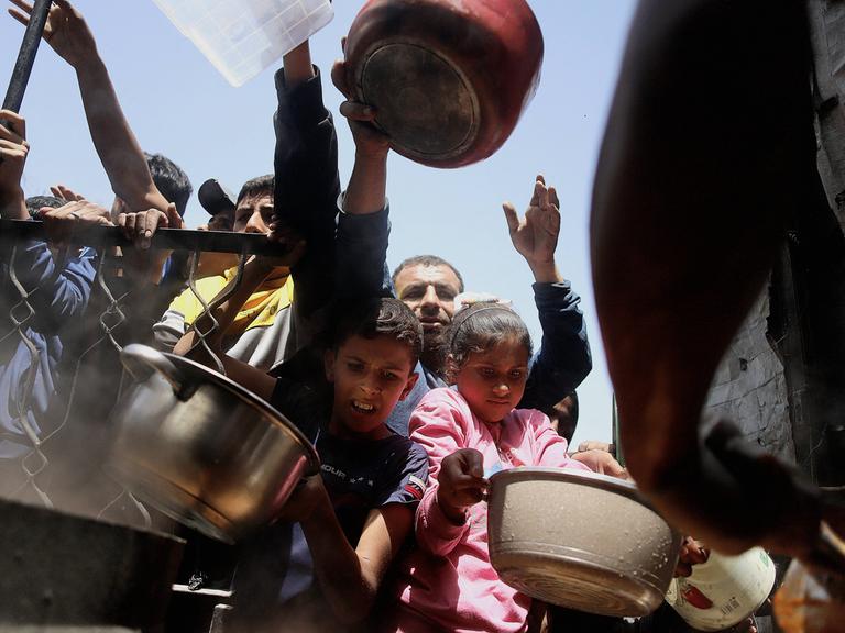 Menschen, Erwachsene und Kinder mit Schüsseln warten darauf, Hilfsgüter im Gazastreifen entgegenzunehmen.
