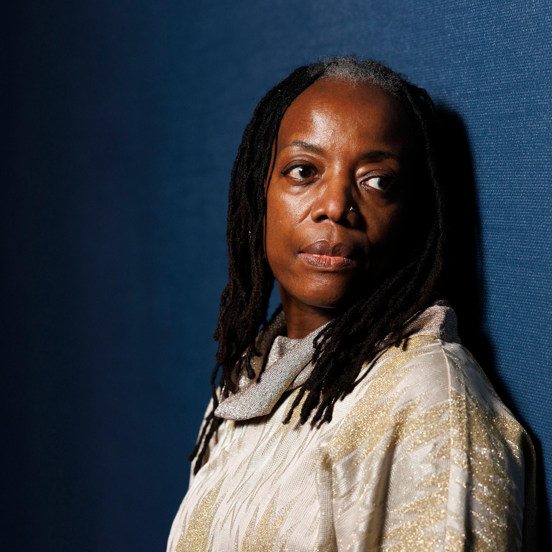 Schriftstellerin Tsitsi Dangarembga blickt vor dunkelblauem Hintergrund nachdenklich in die Kamera.