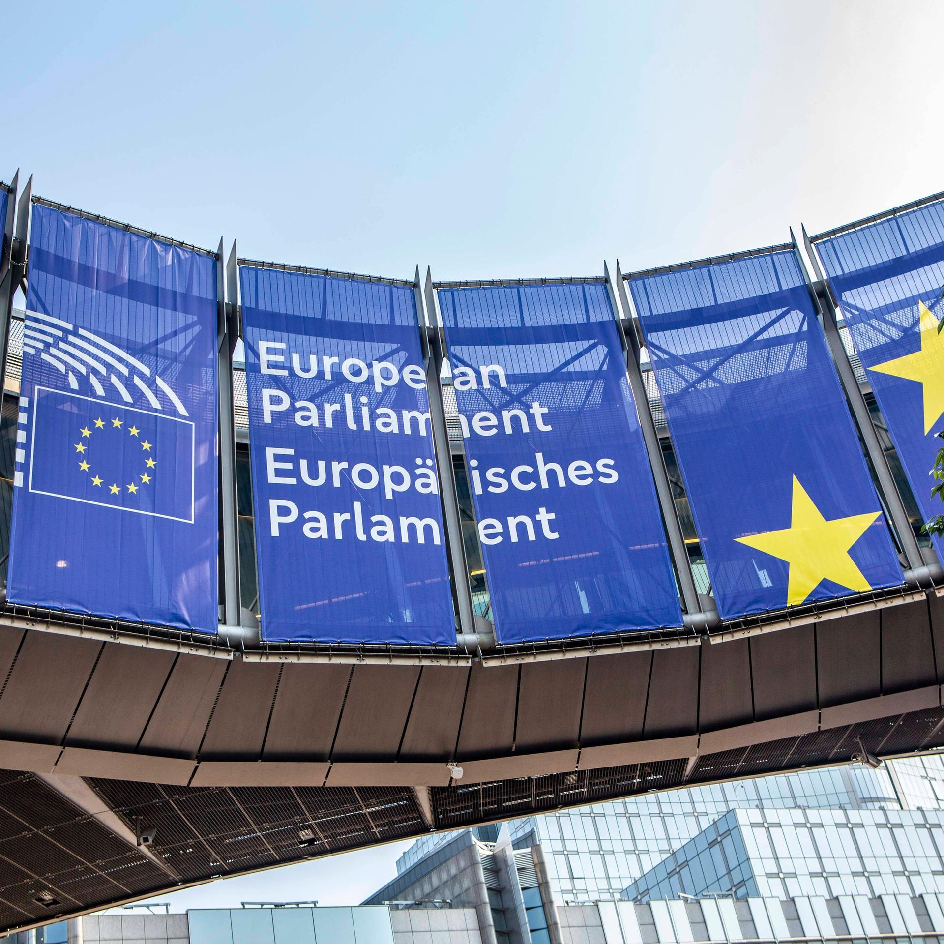 Vor dem Europäischen Parlament hängen blaue Transparente mit dem Namen und Logo des Parlaments. 