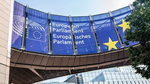 Vor dem Europäischen Parlament hängen blaue Transparente mit dem Namen und Logo des Parlaments. 