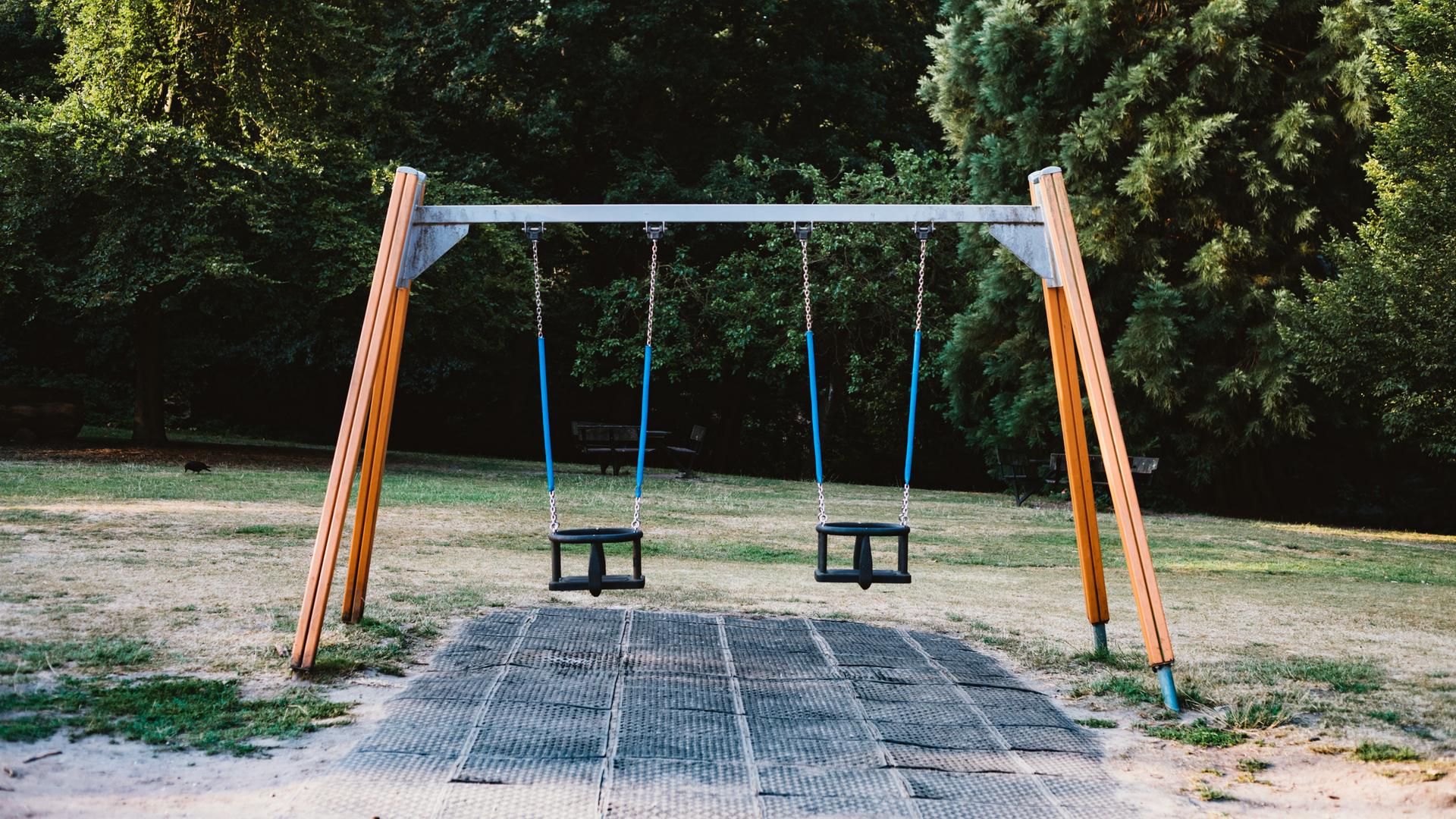 Auf einem Spielplatz steht ein Gestell mit zwei Schaukeln, die beide nicht besetzt sind.
