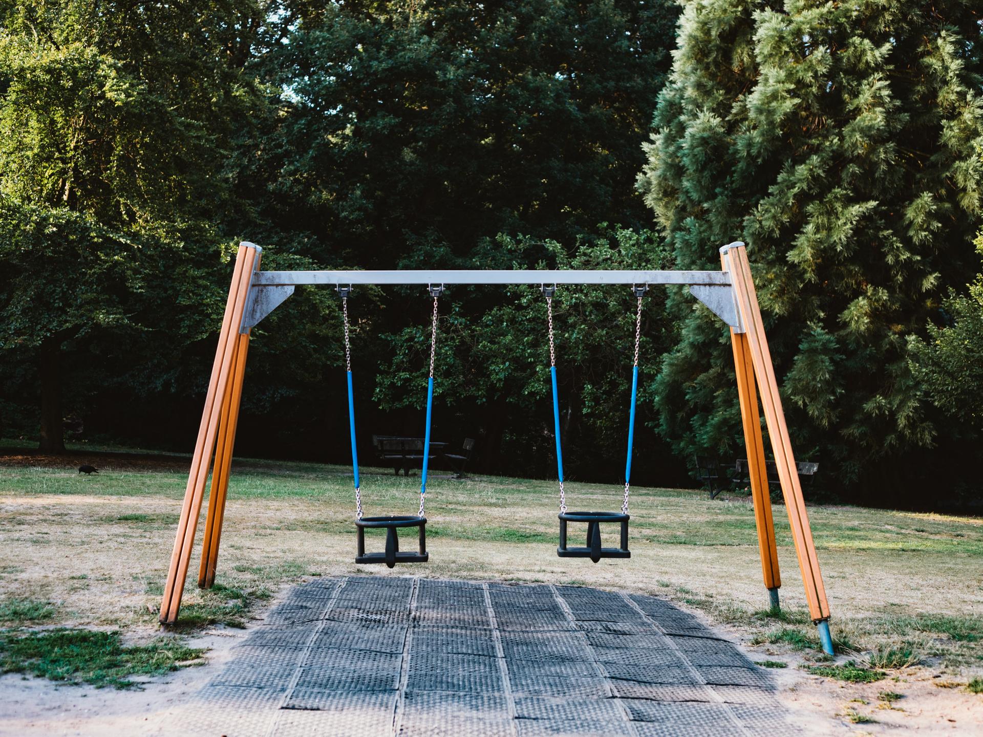 Auf einem Spielplatz steht ein Gestell mit zwei Schaukeln, die beide nicht besetzt sind. Auf einem Spielplatz steht ein Gestell mit zwei Schaukeln, die beide nicht besetzt sind.