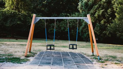 Auf einem Spielplatz steht ein Gestell mit zwei Schaukeln, die beide nicht besetzt sind. Auf einem Spielplatz steht ein Gestell mit zwei Schaukeln, die beide nicht besetzt sind.