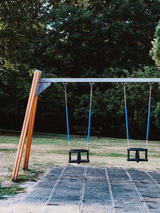 Auf einem Spielplatz steht ein Gestell mit zwei Schaukeln, die beide nicht besetzt sind. Auf einem Spielplatz steht ein Gestell mit zwei Schaukeln, die beide nicht besetzt sind.