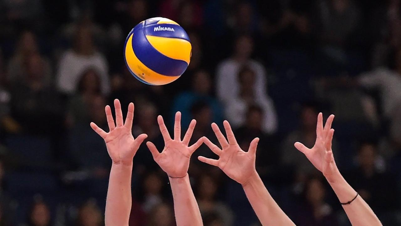 Vier Hände strecken sich nach einem Volleyball.