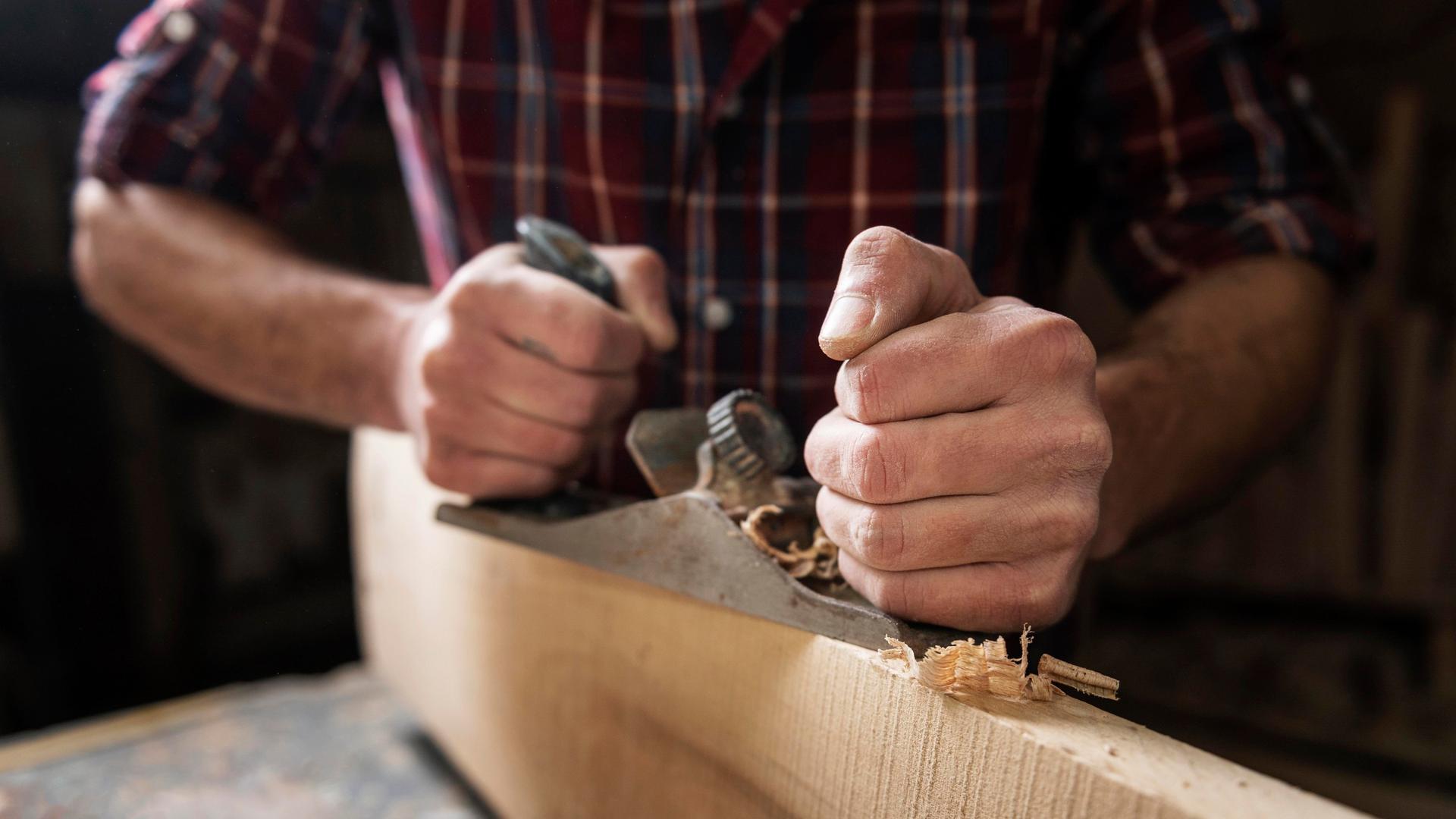 Ein Mann arbeitet an einer Werkbank mit Holz und Hobel.