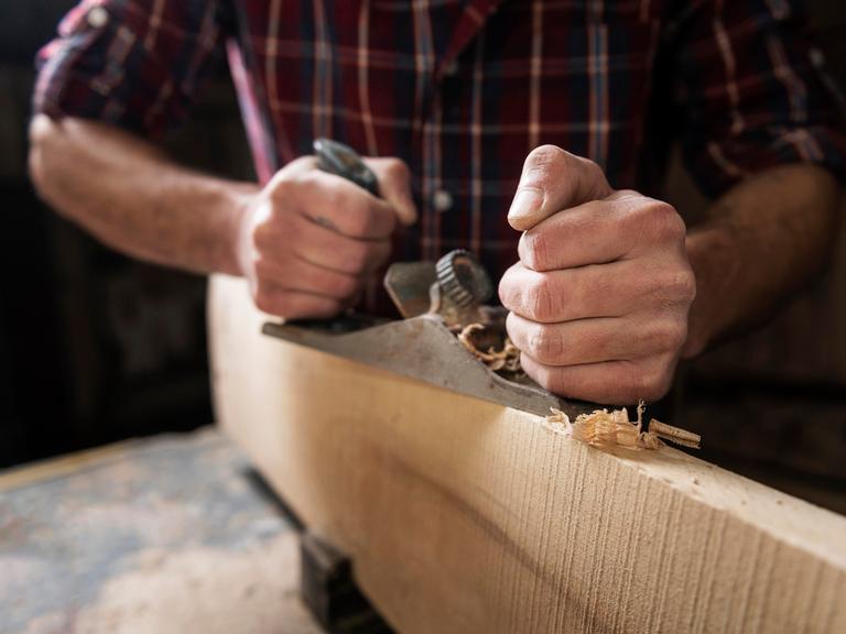 Ein Mann arbeitet an einer Werkbank mit Holz und Hobel.