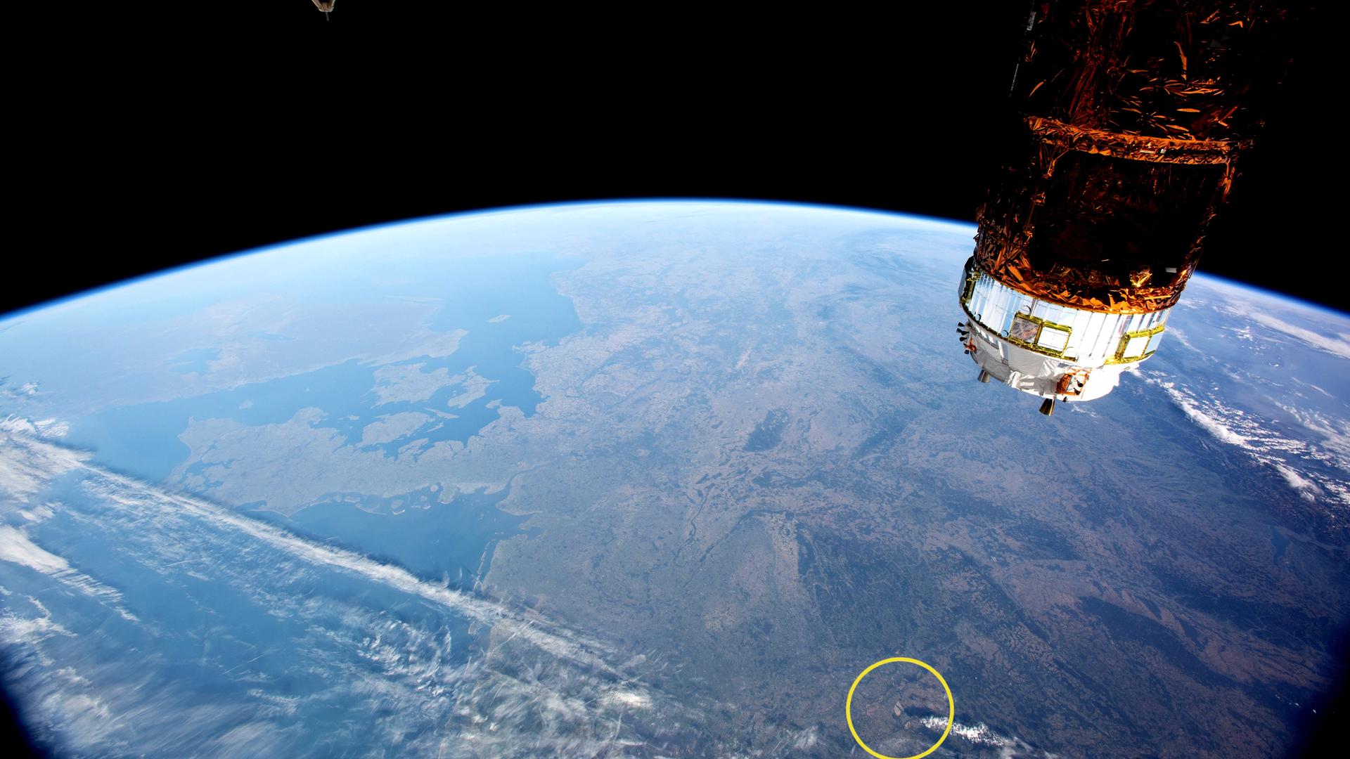 Man sieht groß die obere Hälfte der blauen Erdkugel vor dem schwarzen All. Am rechten Bildrand ein Teil des ISS.