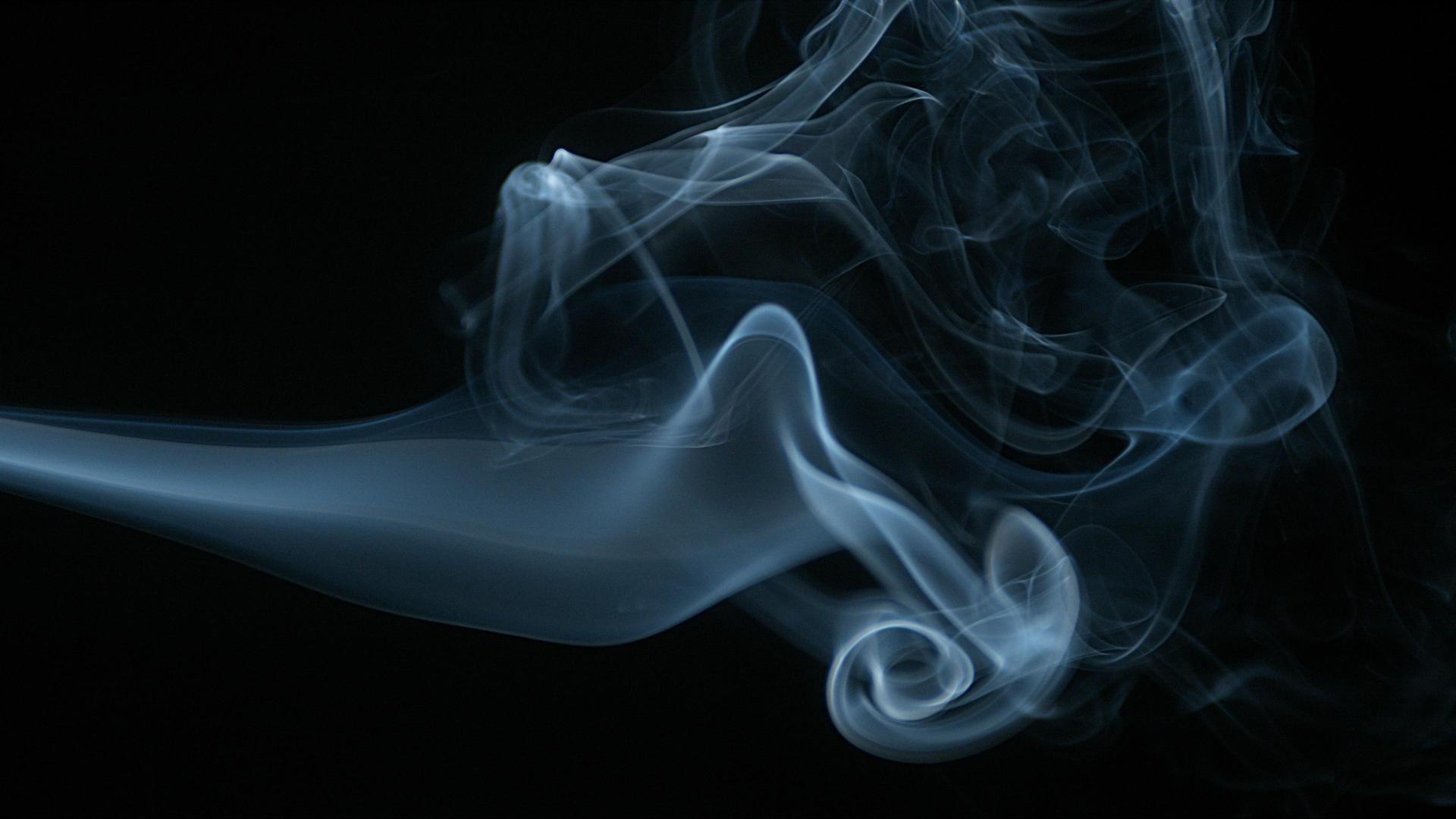 Rauch einer Zigarette steigt gegen schwarzen Hintergrund auf