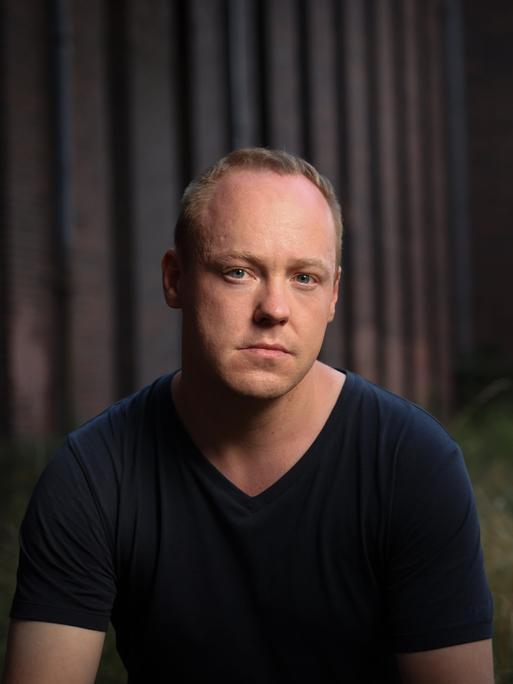 Christian Baron mit kurzen blonden Haaren guckt nach vorne gelehnt und ernst in die Kamera.