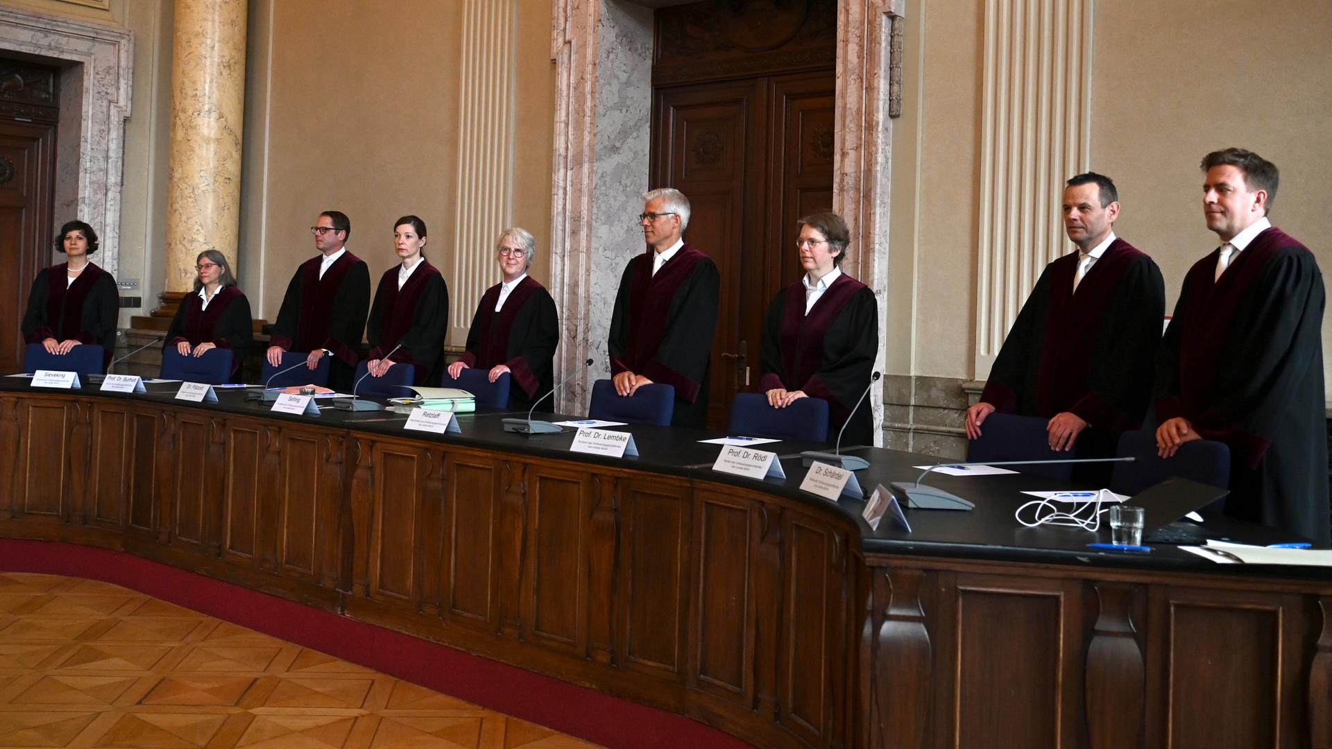 Die Richterinnen und Richter in schwarzen Roben stehen nebeneinander hinter der langen Richterbank in einem Gerichtssaal mit marmorverkleideten Wänden.