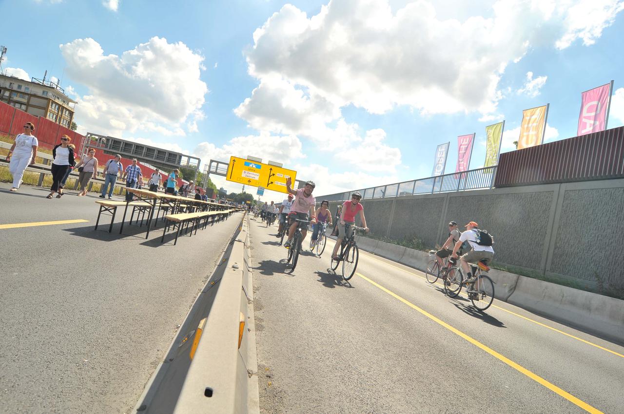 Auf der A40 sind Bierbänke, Fußgänger und Radfahrer bei Sonnenschein zu sehen