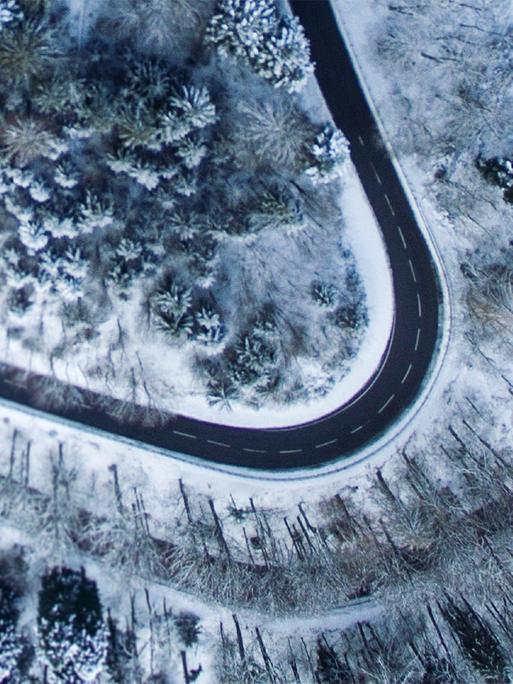 Eine sich schlängelnde Straße in verschneiter Waldlandschaft aus der Vogelperspektive.