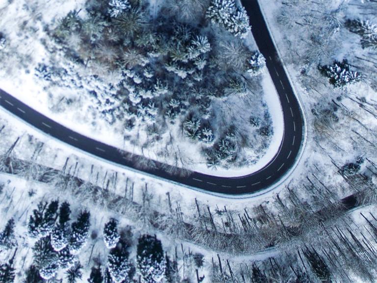 Eine sich schlängelnde Straße in verschneiter Waldlandschaft aus der Vogelperspektive.