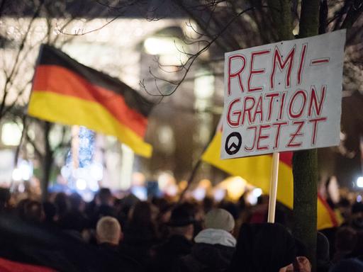 Teilnehmer einer Demonstration rechter Gruppen stehen mit einem Schild mit der Aufschrift "Remigration Jetzt" vor dem Bundeskanzleramt in Berlin. 