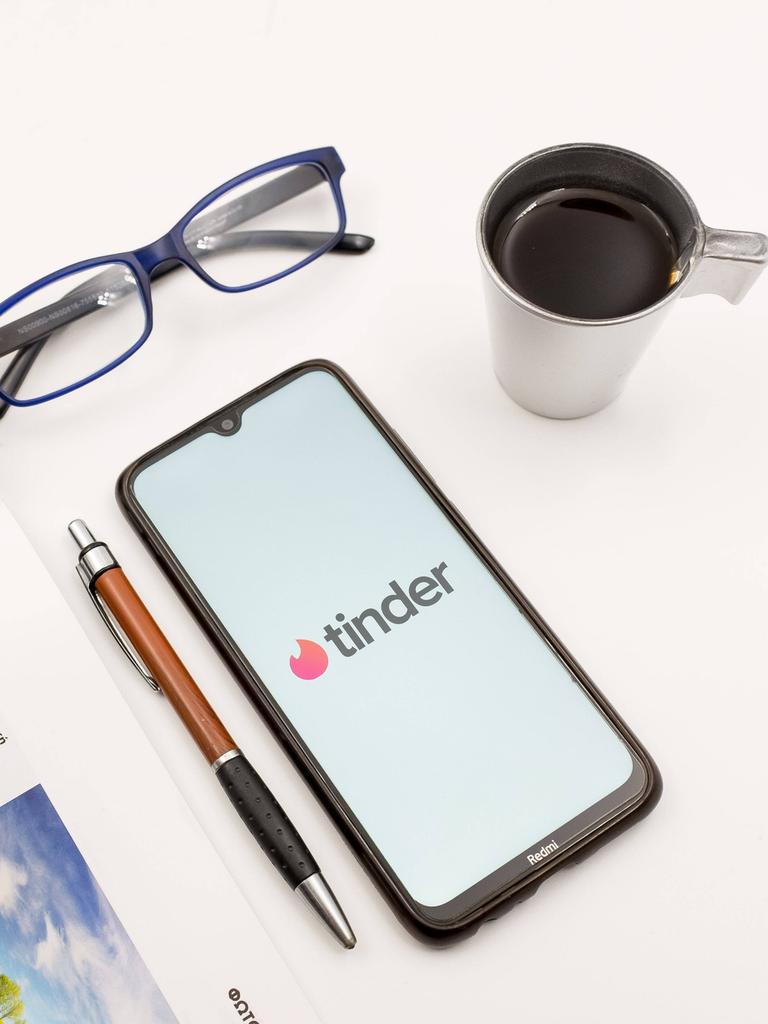 Ein Tisch mit einem Magazin, einem Stift, einer Briller und einem Smartphone auf dem Tinder zu sehen ist.