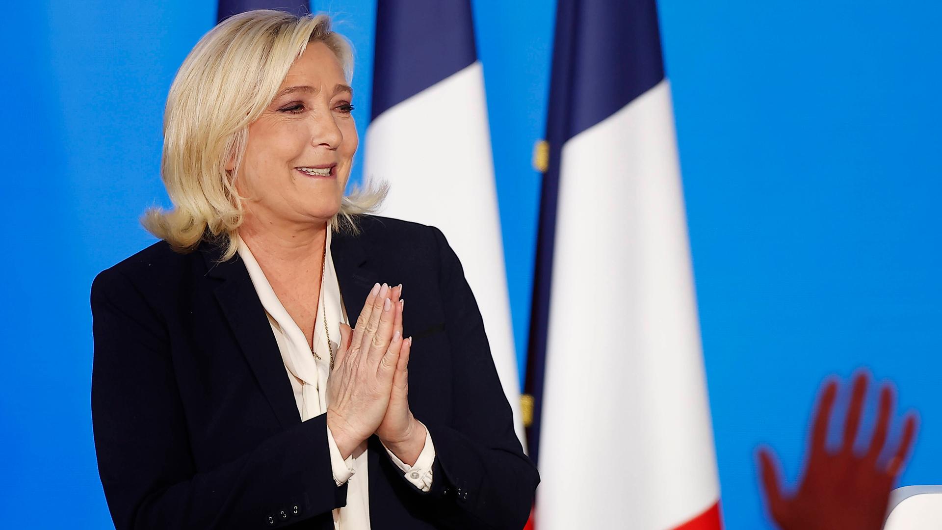 Marine Le Pen steht bei einer Kundgebung des Rassemblement National vor zwei französischen Fahnen Marine Le Pen steht bei einer Kundgebung des Rassemblement National vor zwei französischen Fahnen