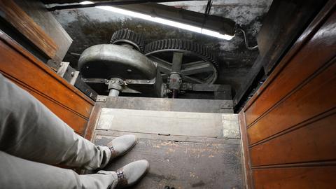 Blick aus der Kabine des Hamburger Paternosters: Unten im Schacht ist der Maschinenraum mit mehreren Zahnrädern zu sehen.