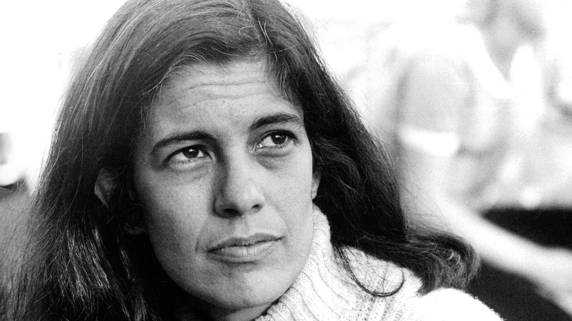 Die Archivaufnahme der 1933 geborenen Intellektuellen Susan Sontag entstand in Stockholm am 6. august 1970. Sie zeigt die Frau mit weißem Rollkragenpulli und langen dunklen Haaren. Sie schaut links an der Kamera vorbei in die Ferne.  