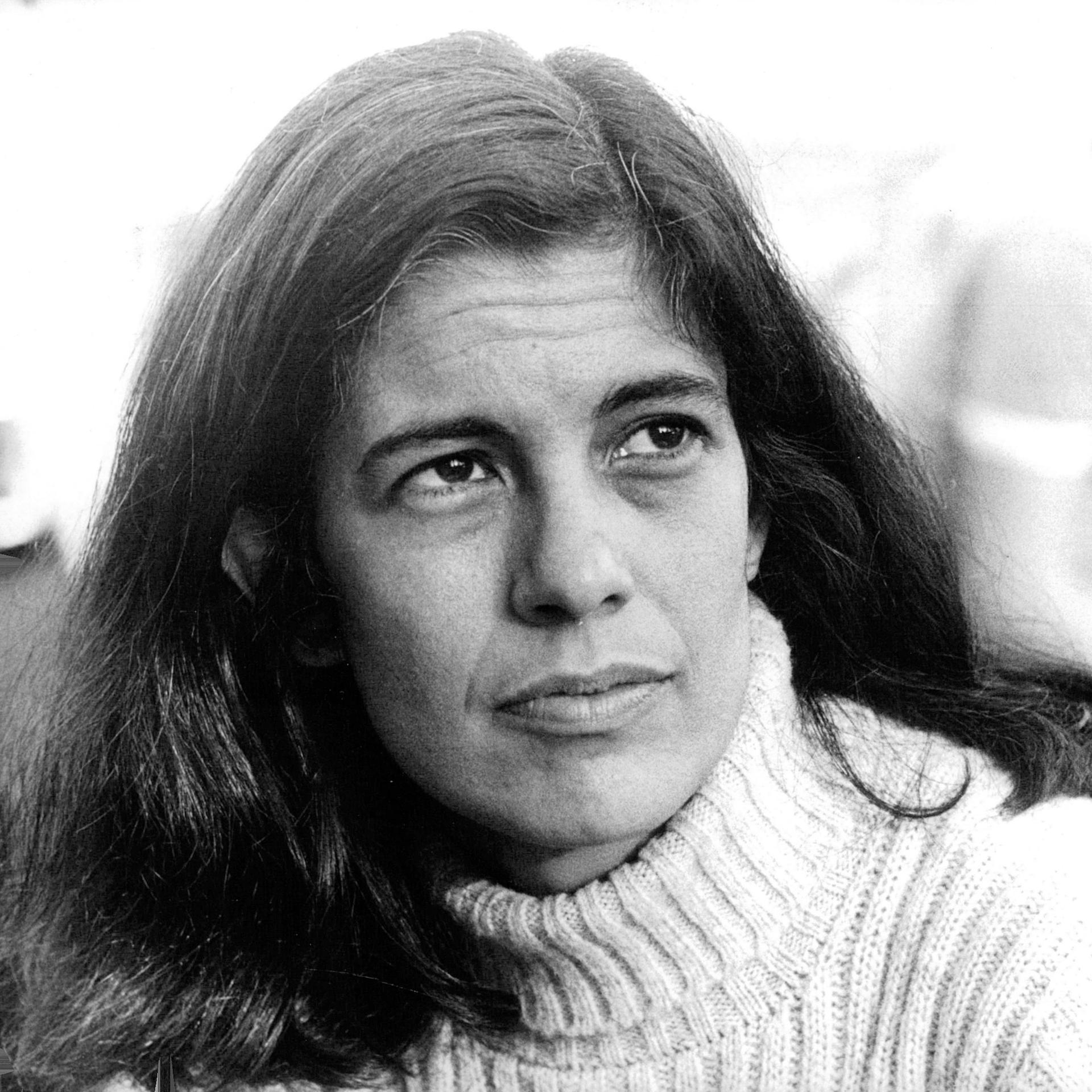 Die Archivaufnahme der 1933 geborenen Intellektuellen Susan Sontag entstand in Stockholm am 6. august 1970. Sie zeigt die Frau mit weißem Rollkragenpulli und langen dunklen Haaren. Sie schaut links an der Kamera vorbei in die Ferne.  