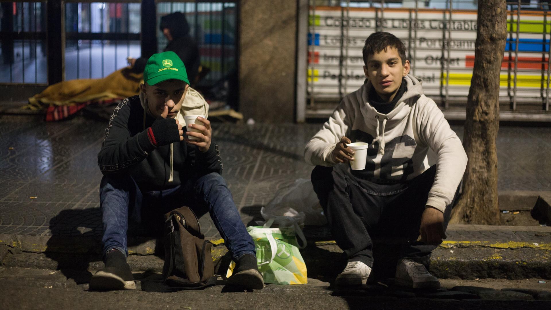 Zwei Jugendliche sitzen mit ihren Habseligkeiten am Straßenrand. Zwei Jugendliche sitzen mit ihren Habseligkeiten am Straßenrand.