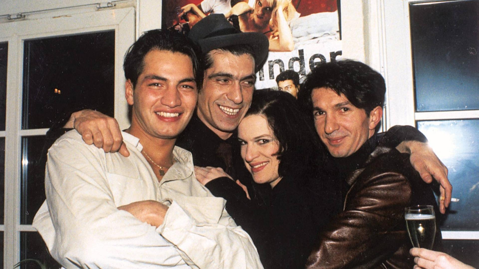 Yüksel Yavuz und drei Darsteller*innen des Filmes "Aprilkinder" liegen sich lachend in den Armen. Im Hintergrund ist das Filmplakat zu sehen.