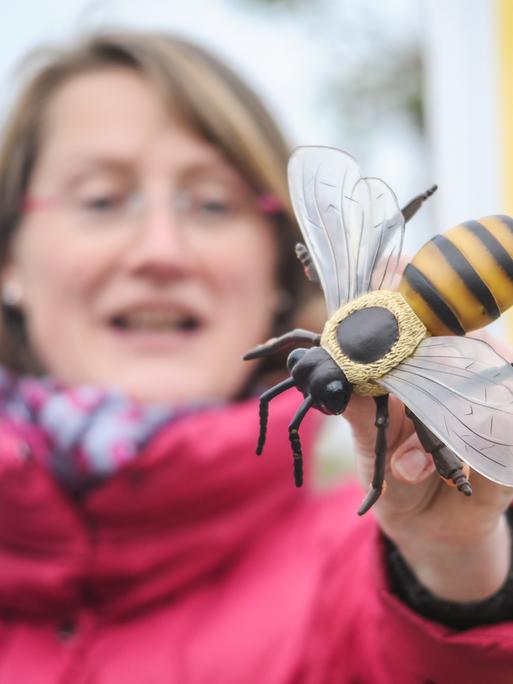 Eine Frau steht vor dem gelben Banner des Landfrauenverbands und hält ein Bienenmodell aus Holz in die Kamera.