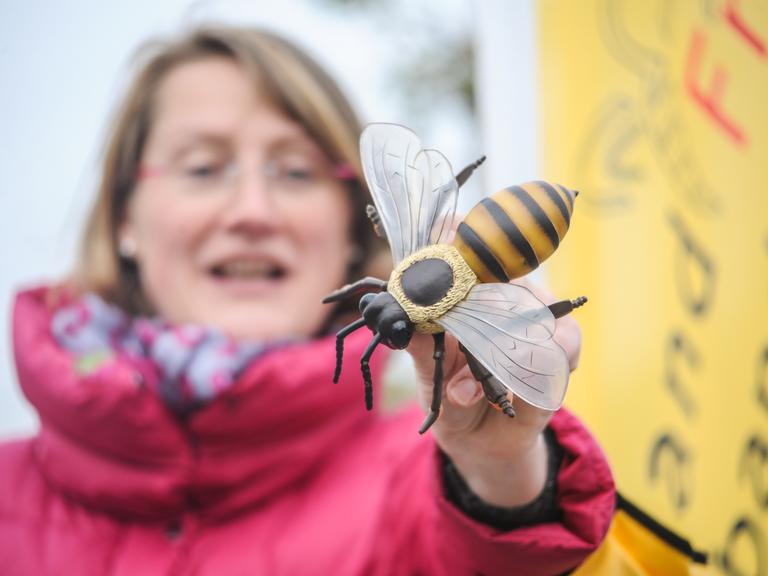 Eine Frau steht vor dem gelben Banner des Landfrauenverbands und hält ein Bienenmodell aus Holz in die Kamera.