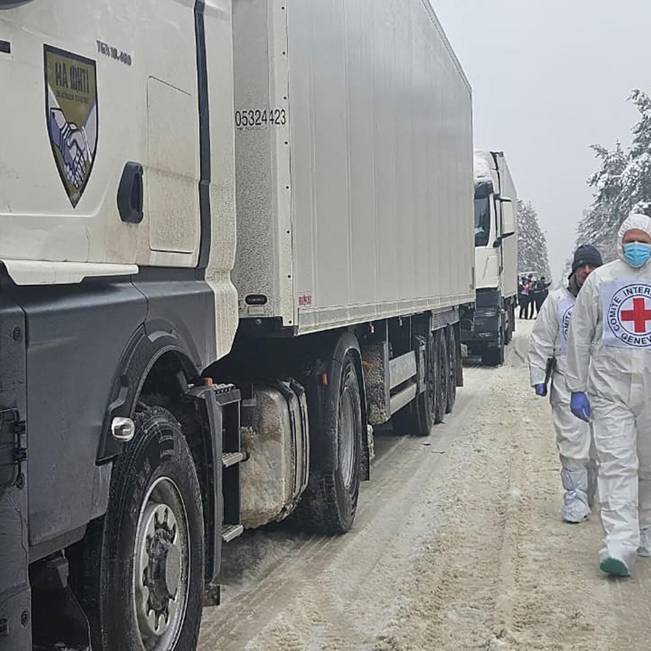 Mitarbeiter des UNHCR laufen neben weißen Lkw's.
