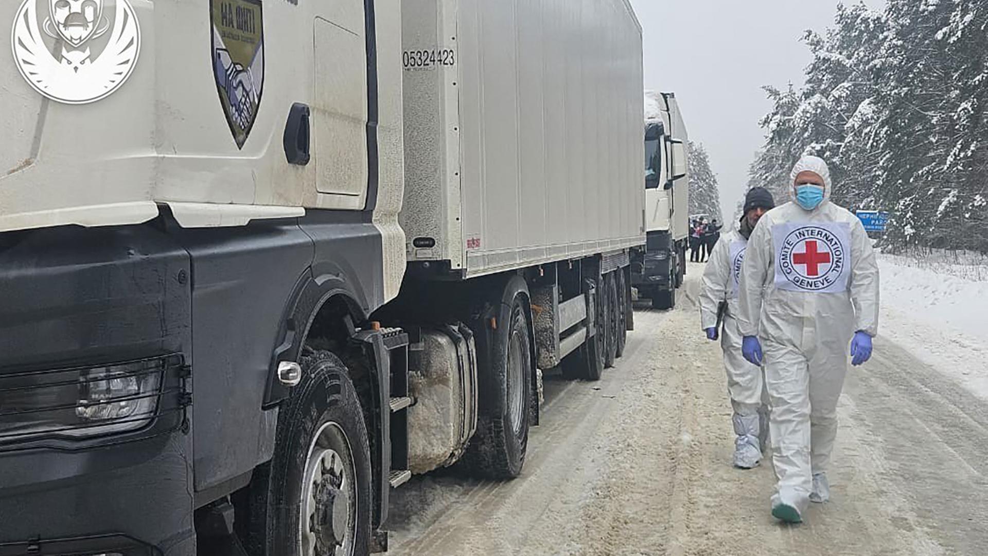 Mitarbeiter des UNHCR laufen neben weißen Lkw's, sie tragen weiße Schutzanzüge und Gesichtsmasken. Mitarbeiter des UNHCR laufen neben weißen Lkw's, sie tragen weiße Schutzanzüge und Gesichtsmasken.