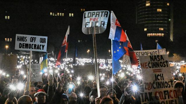 Viele Menschen halten bei einer Demonstration in der Dunkelheit in Bratislava ihre Handylichter nach oben und tragen Plakate, auf einem steht: "Hands off our democracy."