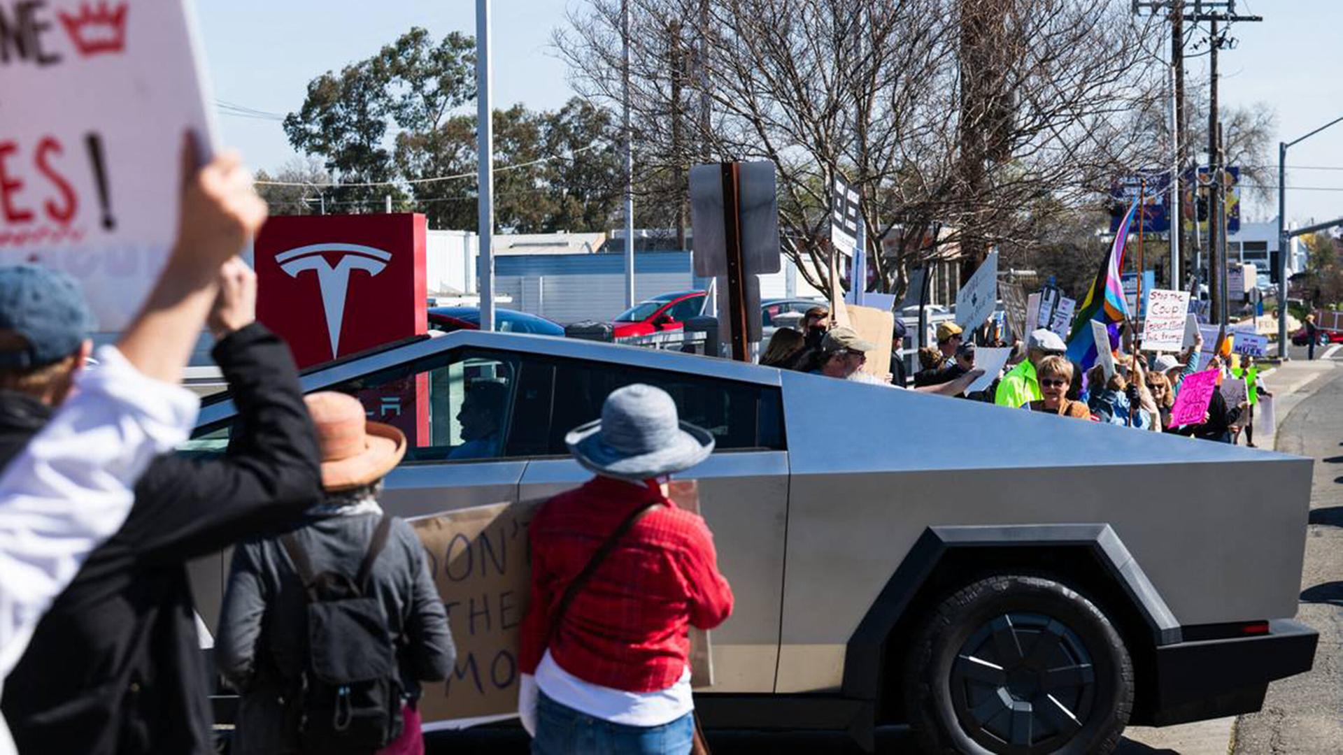 Ein Cybertruck fährt auf ein Tesla Verkaufsgelände im kalifornischen Sacramento. Demonstranten protestieren  gegen den Tech-Billionär und Trump-Gefährten Elon Musk.