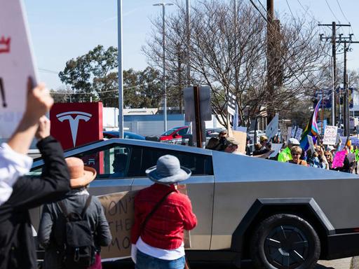 Ein Cybertruck fährt auf ein Tesla Verkaufsgelände im kalifornischen Sacramento. Demonstranten protestieren  gegen den Tech-Billionär und Trump-Gefährten Elon Musk.