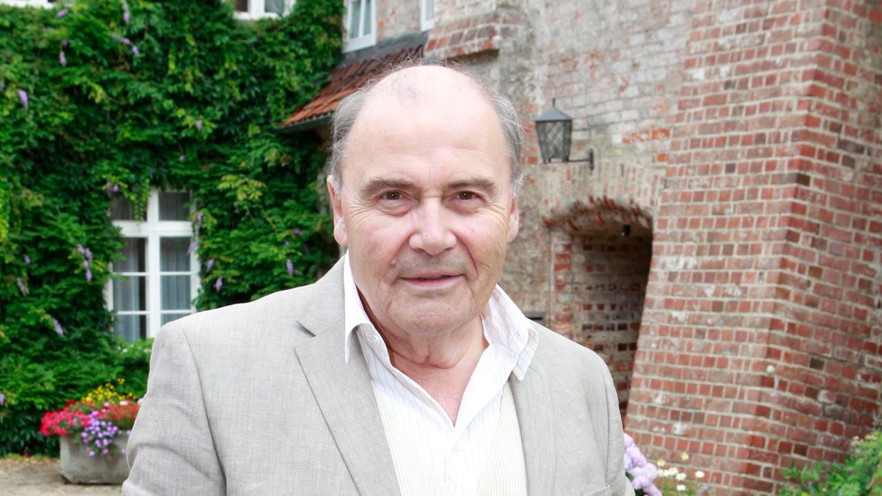 Lambert Hamel steht vor einer Burg. Er schaut in die Kamera.