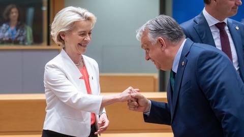 Die Präsidentin des Europäischen Rates Ursula Von Der Leyen und der ungarische Ministerpräsident Viktor Orban am runden Tisch während des informellen EU-Gipfels. Sie reicht ihm eine Hand, er verbeugt sich leicht. 
